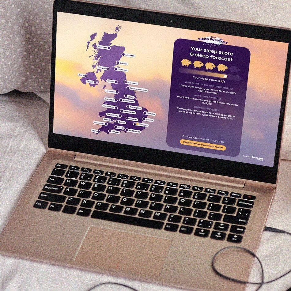 A sleek gold laptop sits open on a soft, rumpled bed sheet, displaying a vibrant sleep score application. The screen features a map of the UK alongside colourful icons, while warm hues of purple and orange create a calming atmosphere, inviting users to explore their sleep data.
