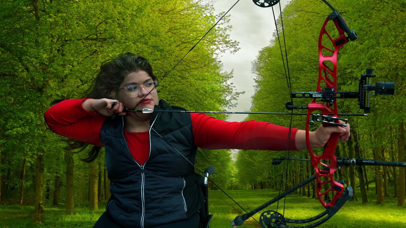 A young woman with long, dark hair is poised in a focused stance, drawing a bright red compound bow. She wears a fitted black vest over a red top, and her glasses reflect the lush greenery around her. Towering trees create a serene backdrop, where vibrant leaves filter soft light, enhancing the dynamic atmosphere.