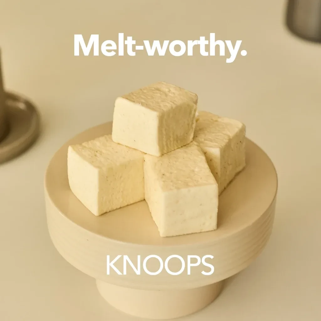 A stylish wooden pedestal displays four creamy white cubes of chocolate, exuding an inviting, melt-in-your-mouth allure. The smooth, matte texture of the cubes contrasts elegantly with the minimalist pedestal, enhanced by soft natural light that accentuates their delicate appearance.