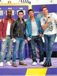 Four men pose against a vibrant backdrop showcasing a purple and yellow colour scheme. The first, in a red checked shirt, stands confidently beside a man in a black leather jacket. The third sports a denim jacket over a white shirt, while the fourth wears a graphic tee with denim jeans. The scene exudes a lively, modern vibe.