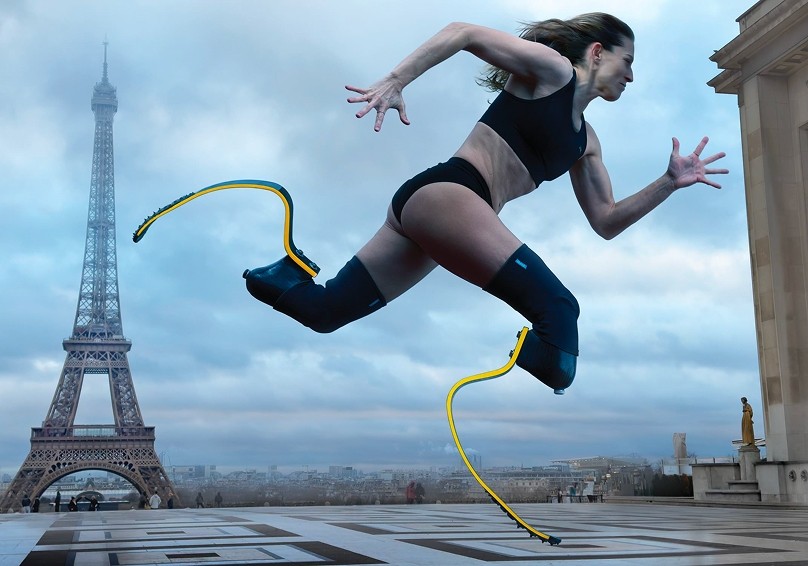 A determined woman strides forward in mid-run, showcasing sleek, adaptive leg prosthetics that extend dynamically behind her. Clad in a black sports bra and shorts, she races against a backdrop featuring the iconic Eiffel Tower, framed by a cloudy sky that adds an ethereal atmosphere.