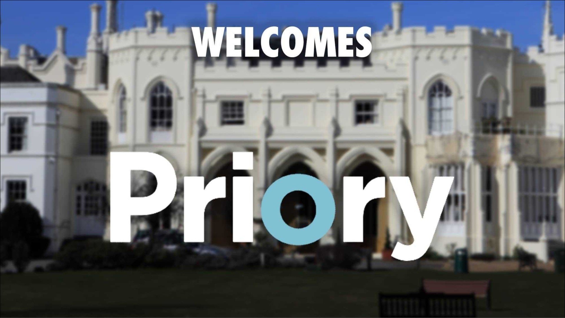 An ornate building serves as a backdrop for the words "WELCOME" and "Priory". The elegant façade features intricate stonework and gothic-style windows, bathed in bright sunlight. A lush green garden surrounds the structure, adding vibrancy and framing this welcoming scene.