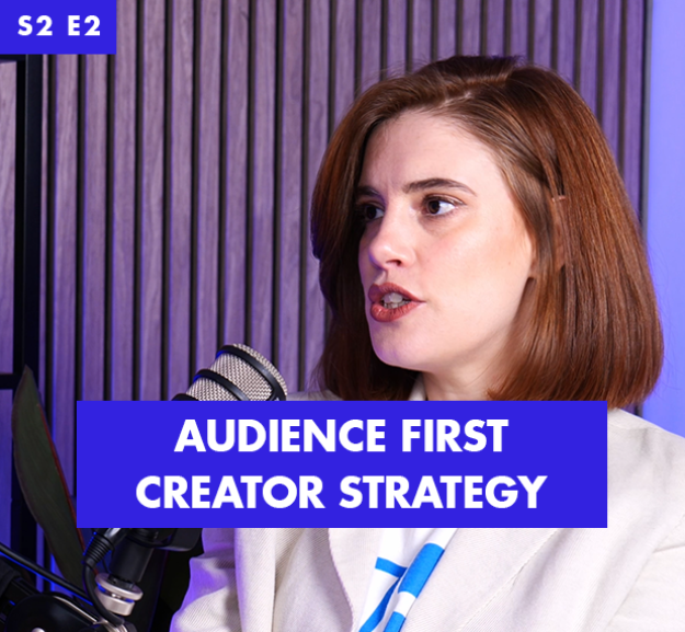 A woman with shoulder-length auburn hair speaks intently into a microphone, set against a backdrop of textured wooden panels. The image features a bold blue and white text overlay that reads, 'AUDIENCE FIRST CREATOR STRATEGY,' accentuating the professional atmosphere.