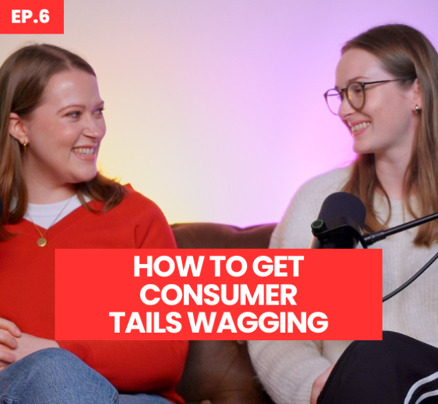 Two women are seated on a plush, brown leather sofa, engaging in conversation. The woman on the left wears a vibrant red sweater paired with blue jeans, while the woman on the right sports glasses and a white oversized knit sweater. A microphone is positioned between them, and bold text overlays the image, stating "HOW TO GET CONSUMER TAILS WAGGING EP.6".