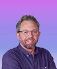 A man with short, wavy hair and a well-groomed beard smiles warmly. He wears clear glasses and a dark button-up shirt, which contrasts with the soft purple gradient background. The image features a polished, modern aesthetic, radiating a friendly and approachable vibe.