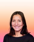 A woman with long, dark hair and a warm smile poses against a soft gradient background of peach and pink hues. She wears a simple black top, highlighting her confident yet approachable presence. The smooth background creates a calming and inviting atmosphere.