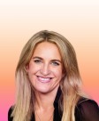 A woman with long, flowing blonde hair smiles warmly against a vibrant gradient background transitioning from soft pink to light orange. She wears a black blouse, enhancing the brightness of her complexion and the lively atmosphere of the image.