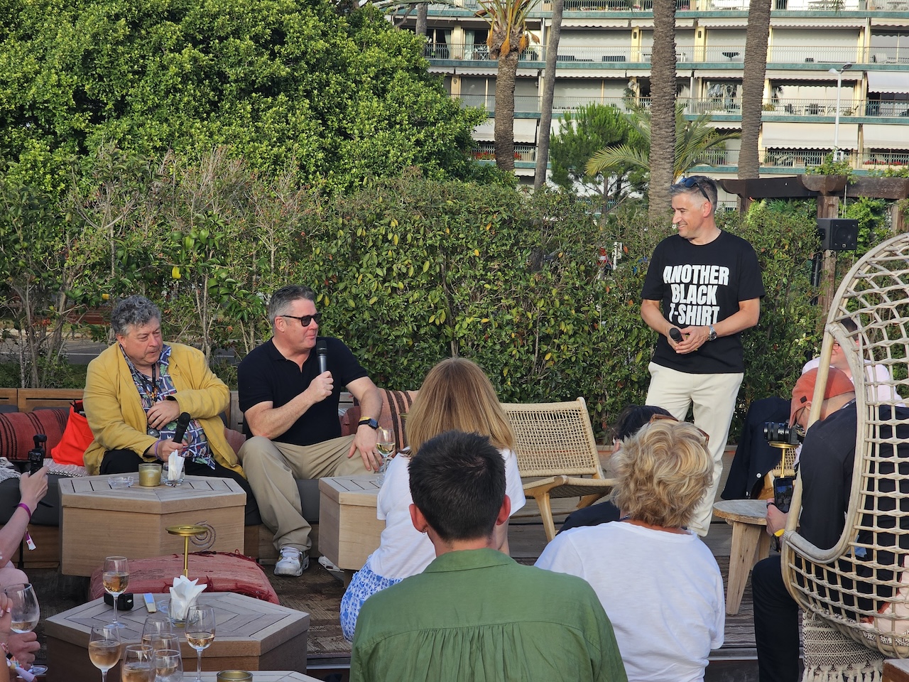 3 men are in discussion in front of an audience whilst sat outside