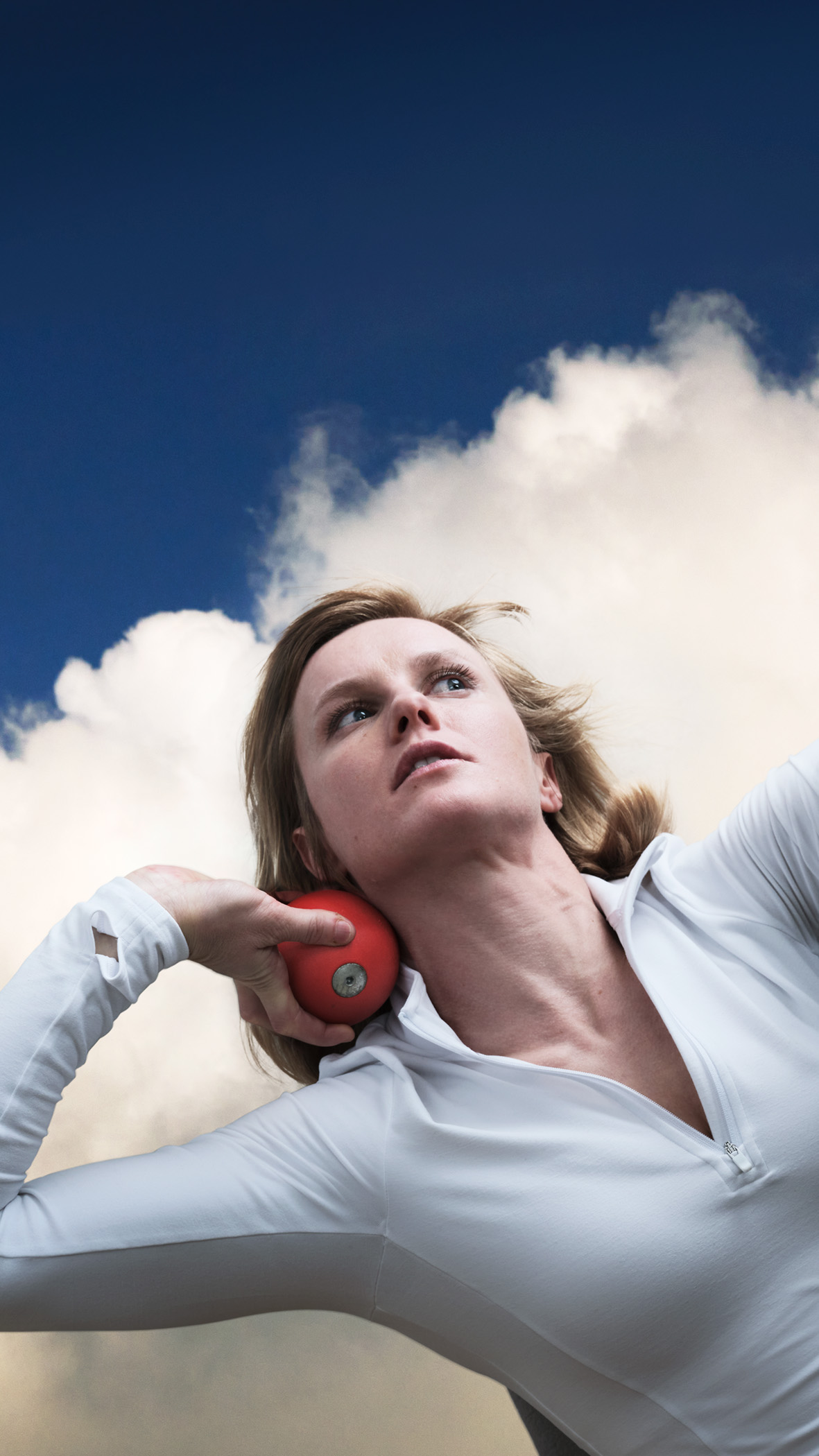 A woman in white holds a shotput