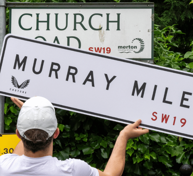 A man replaces a road sign with an Andy Murray Castore sign called Murray Mile