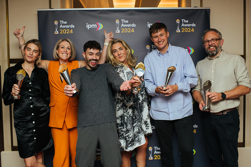 A group of six people, smiling and standing in front of a colorful gradient background. Text above them reads,