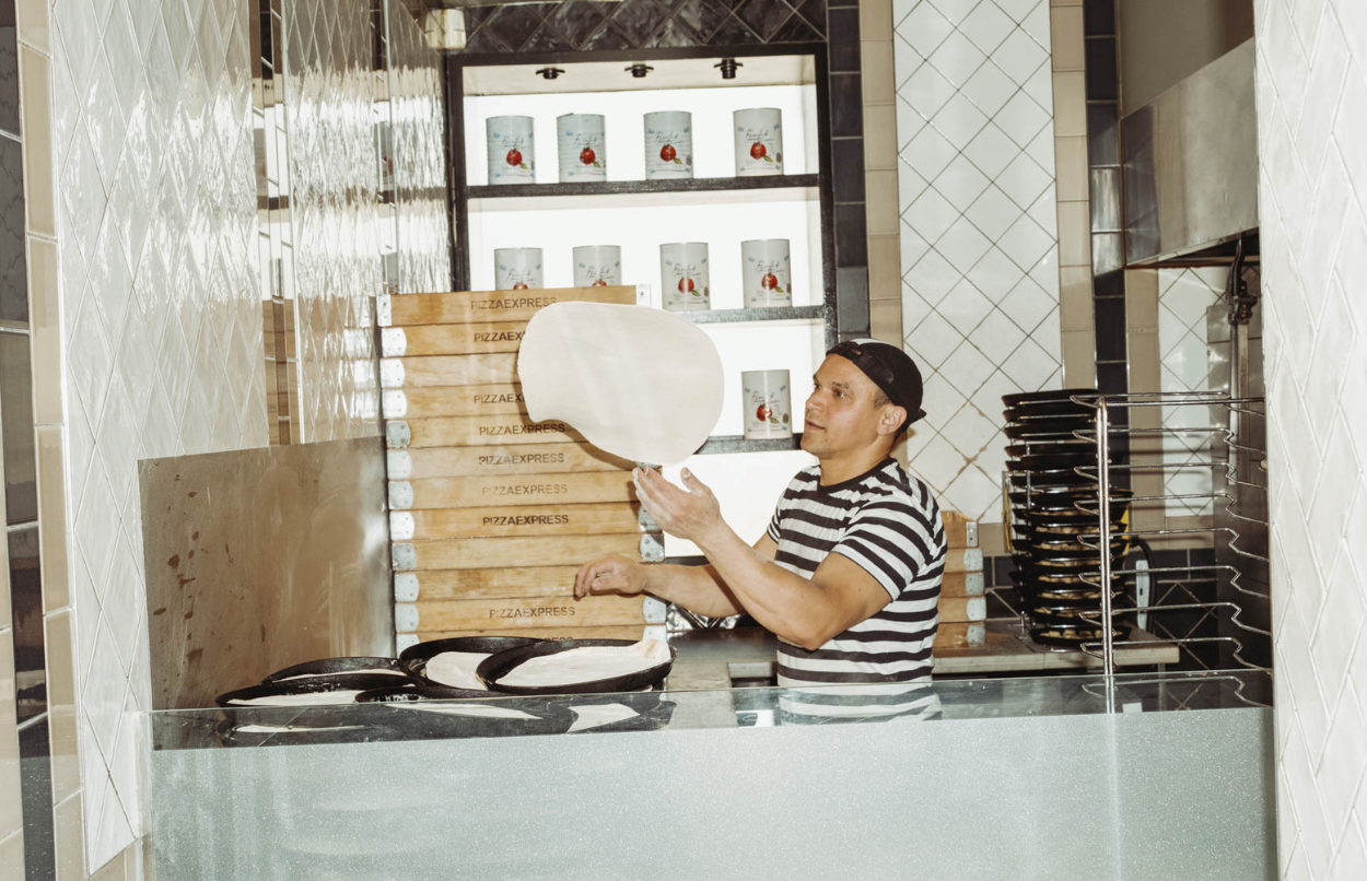 A pizza chef in a stripey shirt in a restaurant is flipping dough