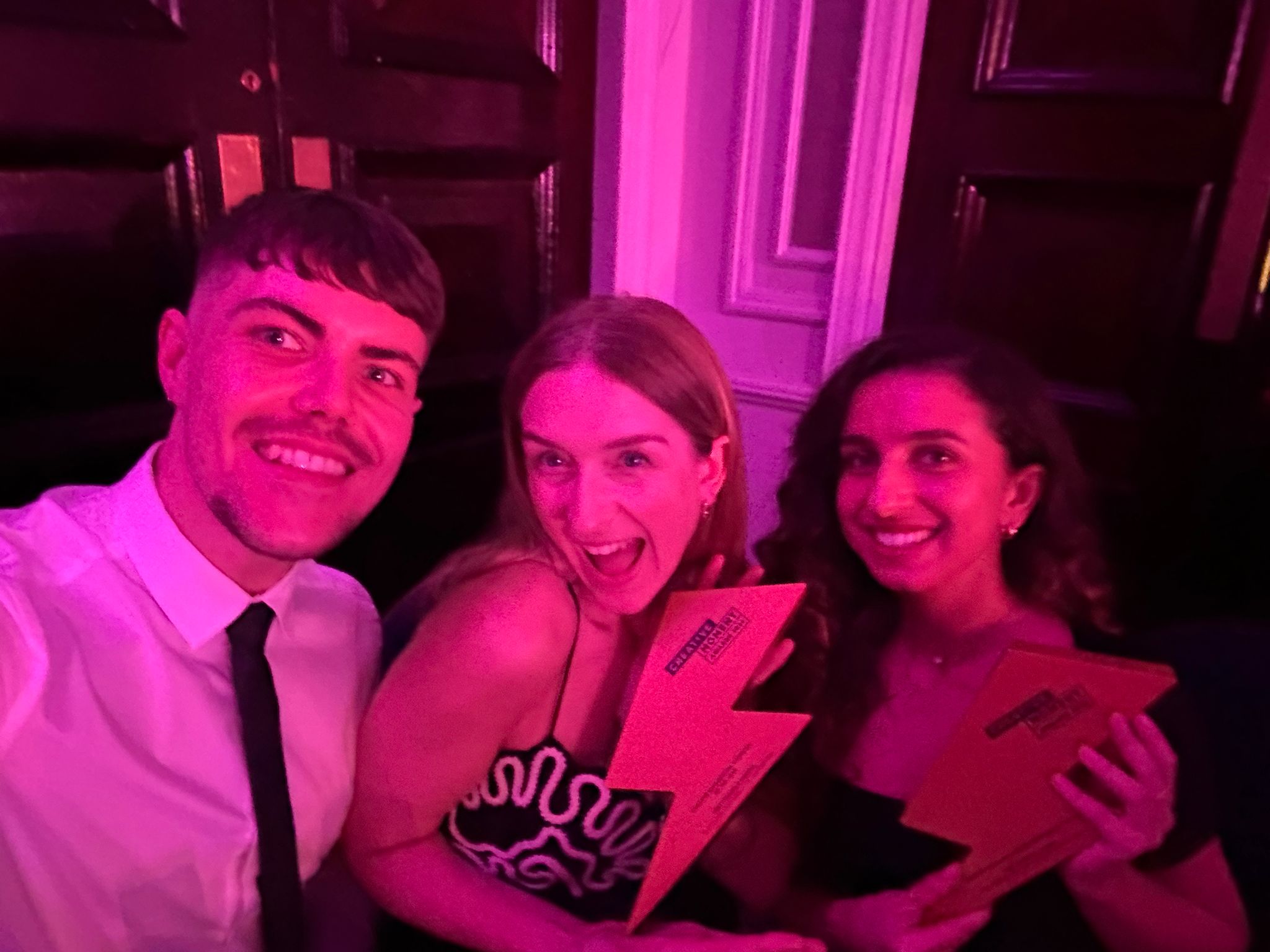A man in a shirt and tie and two women are celebrating an award win