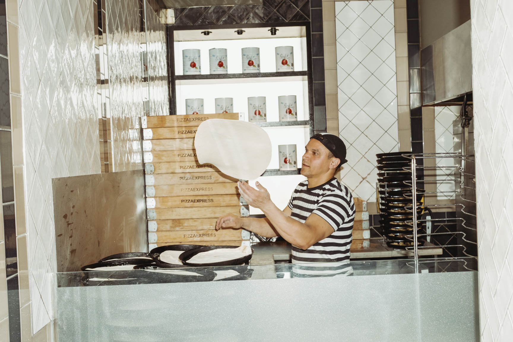 A pizza chef in a stripey shirt in a restaurant is flipping dough