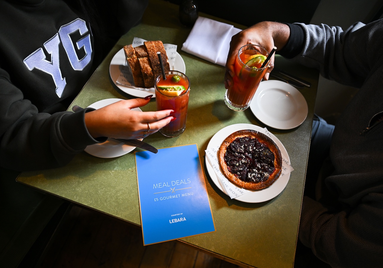 Two hands are holding burgers whilst sat at a table