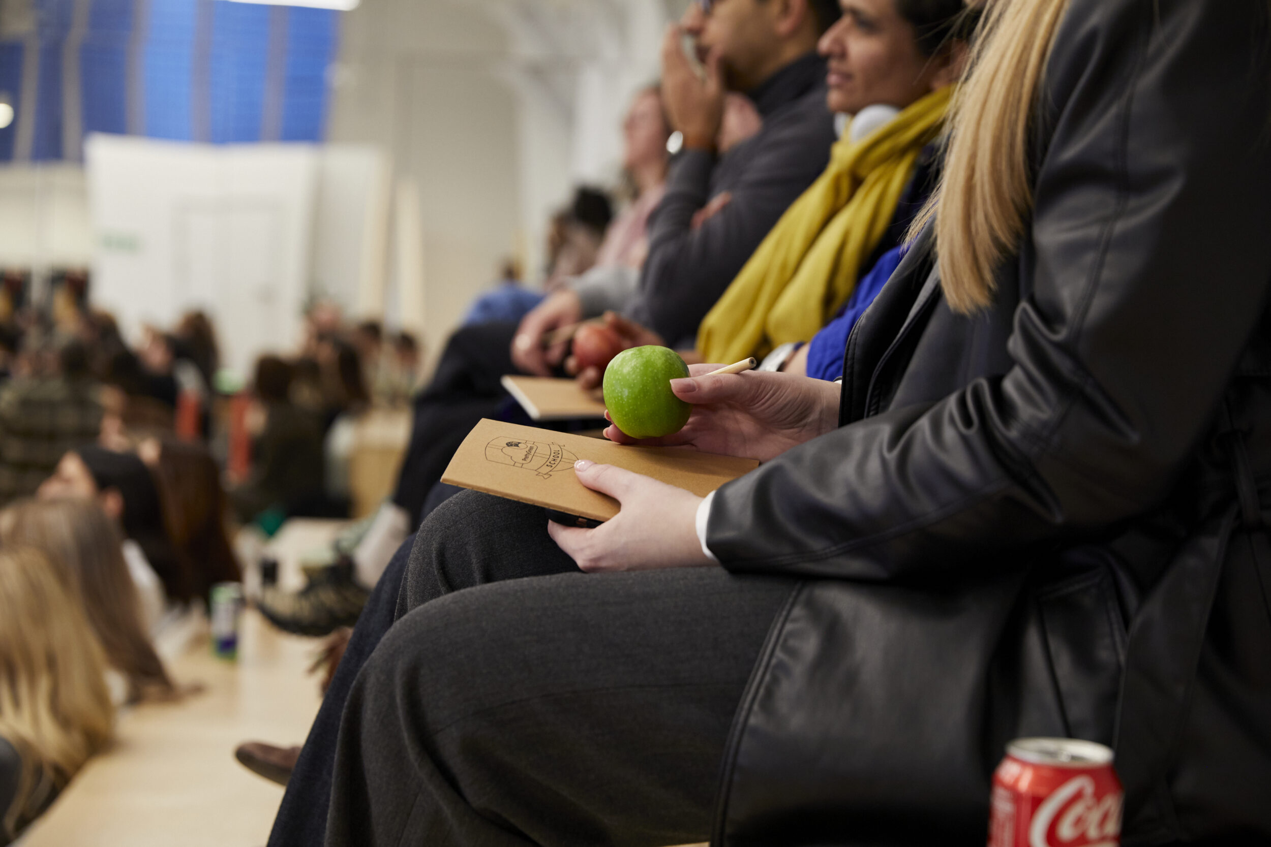 A person is sat holding a notepad and apple