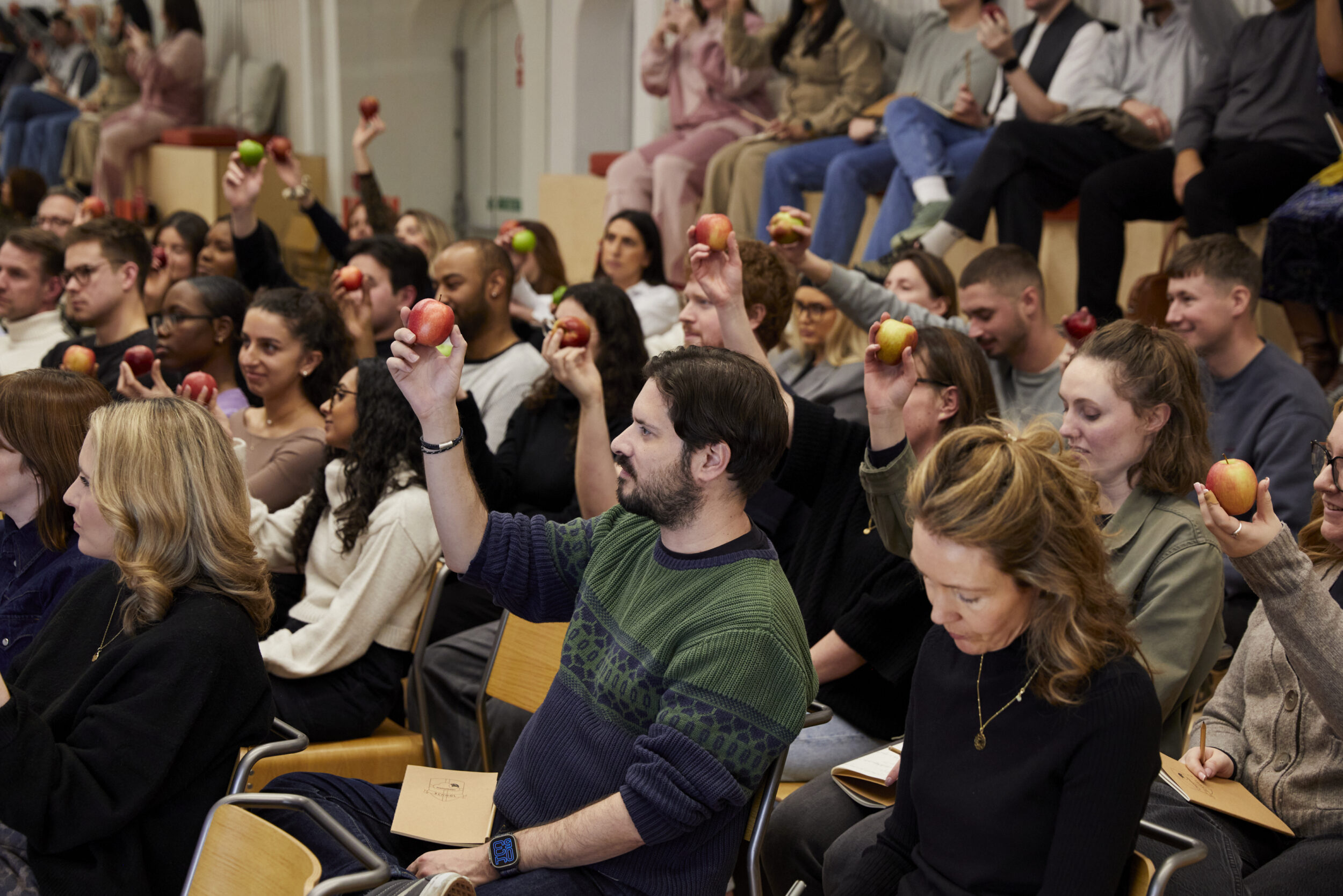 A group of people sat in chairs hold apples up in the air