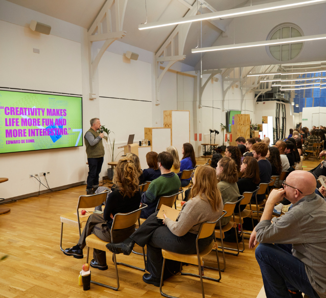 A group of people sit on chairs in a hall watching a presentation,
